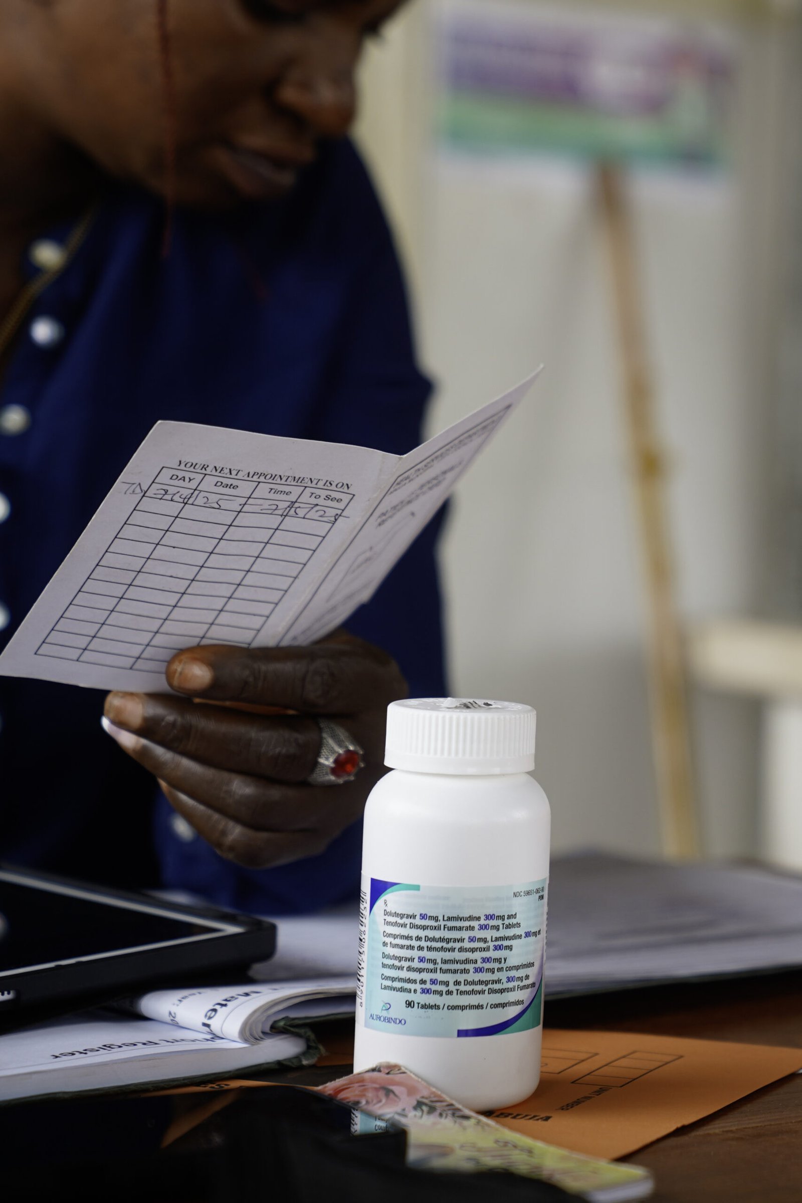 Tina Amos, a health care counsellor, reviews patient records at the Lugbe Primary Health Care Centre in Abuja, Nigeria, as Kyuntu John holds her baby in the background. July 29, 2025. Photograph: Marvellous Durowaiye /CCIJ