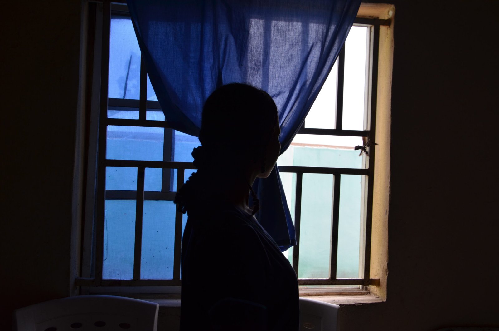 A female volunteer at Njobbore PHC stands while she looks through the window